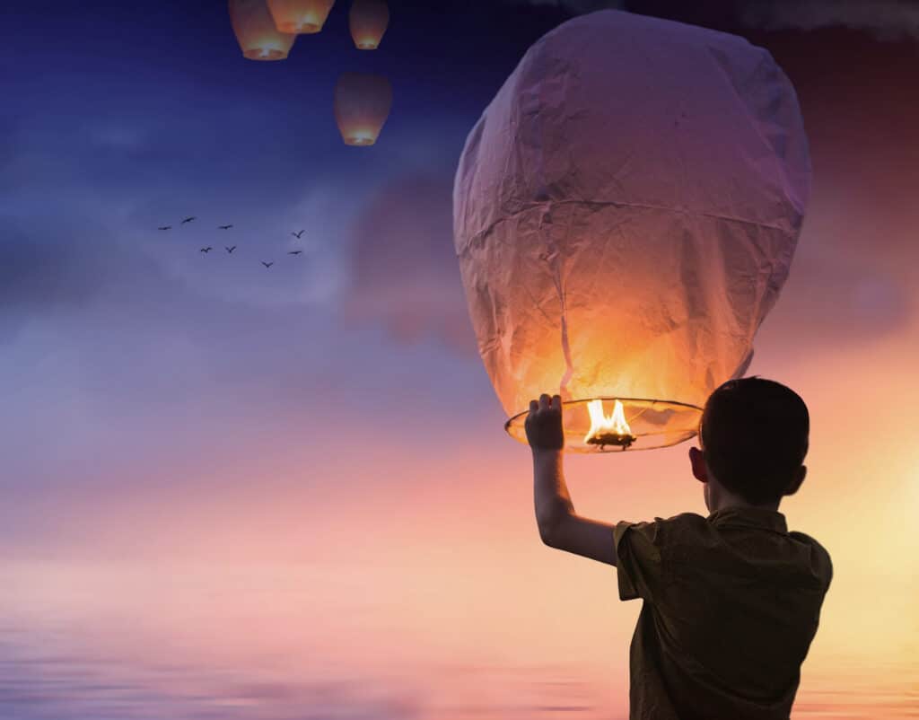 Un enfant lâchant une lanterne céleste à la tombée du jour, métaphore de l'éclairage et de l'ascension dans la systémie familiale et conjugale.